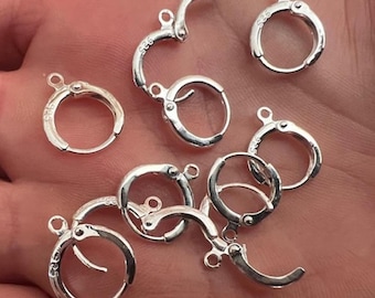 May include: A close-up of a group of silver earring hoops with a clasp closure. The hoops are arranged in a random pattern on a hand.