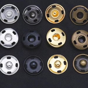 May include: Twelve metal snap buttons in various finishes, including gold, silver, black, and bronze. Each button has four prongs and a raised centre.
