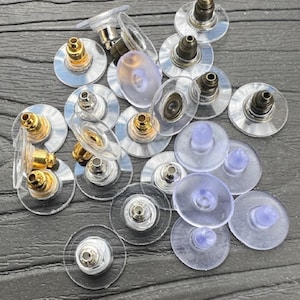 May include: A collection of clear plastic earring backs with gold and silver posts. The backs are designed to be used with stud earrings.
