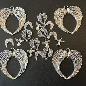 May include: A collection of silver-toned metal angel wing charms, including several pairs of wings in a heart shape, individual wings, and small angel figures. These charms are perfect for jewellery making, scrapbooking, and other craft projects.