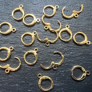 May include: A close-up of a group of gold-toned earring hooks. The hooks are made of metal and have a spring-loaded clasp.