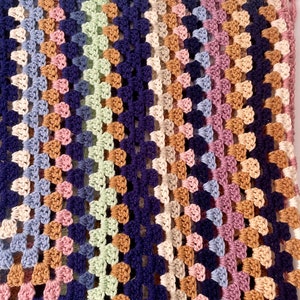 K&ouml;nnte beinhalten: Eine mehrfarbige geh&auml;kelte Decke mit einem diagonalen Muster in Blaut&ouml;nen, Gr&uuml;n, Rosa, Braun und Beige.