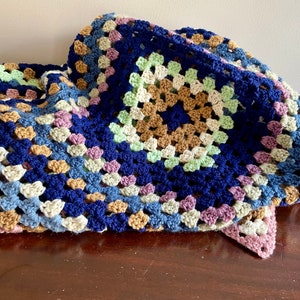 K&ouml;nnte beinhalten: Eine geh&auml;kelte Granny-Square-Decke in Blaut&ouml;nen, Gr&uuml;n, Braun und Rosa.