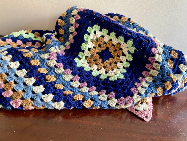 K&ouml;nnte beinhalten: Eine geh&auml;kelte Granny-Square-Decke in Blaut&ouml;nen, Gr&uuml;n, Braun und Rosa.