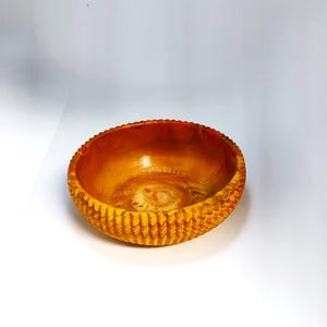 May include: A handcrafted wooden bowl with a warm, amber hue. The bowl features a textured, ridged exterior and a smooth interior. The rim has a decorative, scalloped edge. This decorative bowl is suitable for serving or display.
