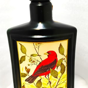 May include: Black rectangular bottle with a black cap. The label features a red bird perched on a branch with green leaves and yellow berries. The text "BEAM KENTUCKY STRAIGHT BOURBON WHISKEY" is at the bottom.