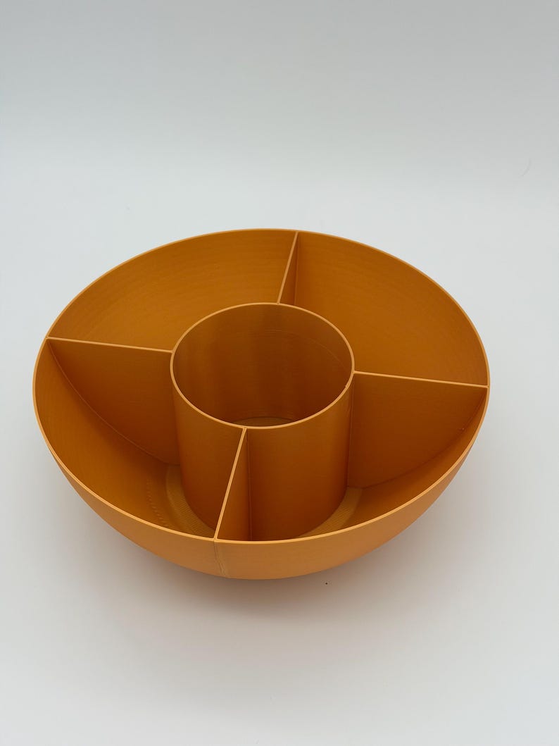 May include: A circular orange storage organizer featuring a central cylindrical compartment surrounded by four distinct wedge-shaped sections. The container has smooth, solid walls and an open top design, providing multiple divided spaces for sorting items.