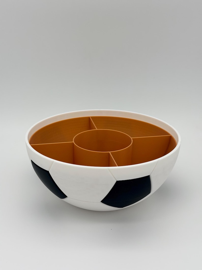 May include: A round, bowl-shaped organizer featuring a white and black exterior patterned like a soccer ball. The interior is a solid tan color and is divided into five distinct sections, including a central circular compartment and four surrounding ones.