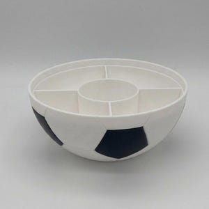 May include: A white and black soccer ball shaped serving bowl with a divided interior. The bowl features a central circular compartment surrounded by four outer sections, mimicking the classic pentagonal pattern of a soccer ball on the exterior.