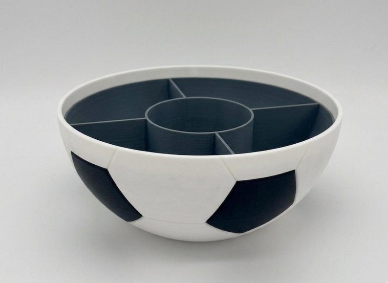 May include: A round bowl with a white and black soccer ball pattern on the exterior. The interior is dark gray and features a central circular compartment surrounded by four separate wedge-shaped sections for organized storage and serving.