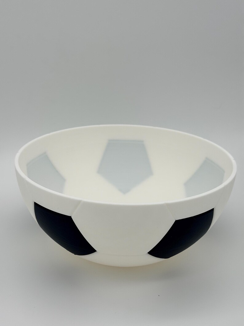 May include: A white bowl featuring a black and gray pentagonal pattern on its exterior and interior, designed to resemble the classic aesthetic of a soccer ball. The bowl has a smooth, rounded shape with a wide opening and a solid base.
