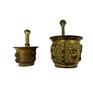 Peut inclure: Deux mortiers et pilons antiques en laiton. Le plus grand ensemble a un bol avec trois visages sculptés sur le côté. Le plus petit ensemble a un bol uni.