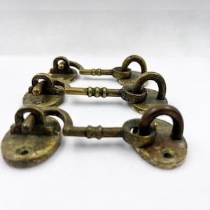 Peut inclure: Trois loquets de porte de cabinet en laiton antique en forme de clé avec des plaques ovales et un motif torsadé décoratif.