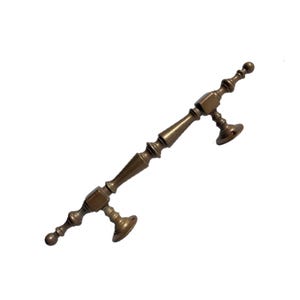 May include: A bronze door pull with an elaborate design. The handle has decorative features, including rounded shapes and tapered sections. The pull has two circular mounting plates. The handle is approximately 25 cm long.