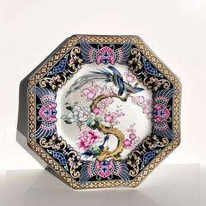 May include: An octagonal decorative plate with a detailed bird and floral design. The plate features a white center with pink flowers and blue birds, framed by a black border with gold accents and ornate patterns.