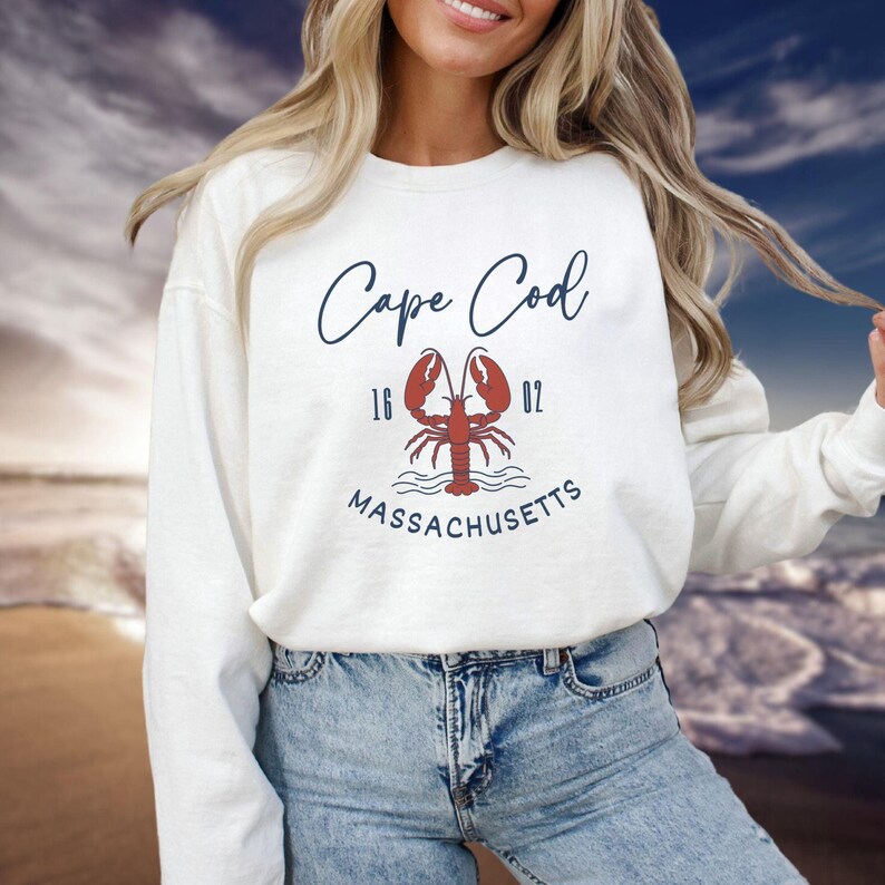 May include: White sweatshirt with a blue and red graphic design of a lobster with the text "Cape Cod 16 02 MASSACHUSETTS" printed on the front.