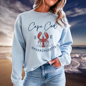 May include: Light blue sweatshirt with the text "Cape Cod" and a red lobster illustration. The text "16 02 MASSACHUSETTS" is below the lobster.