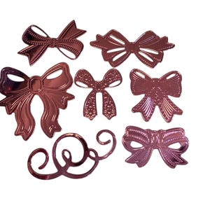 May include: A collection of rose gold-colored decorative bows and a swirl design. The bows vary in style, with some featuring intricate details and others a simpler design. The items are arranged on a white background.