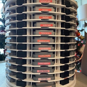May include: A white, multi-tiered storage carousel filled with ink pads. Each level holds several ink pads, with labels like "lumberjack plaid," "barn door," and "victorian velvet." The carousel is designed for organizing craft supplies.