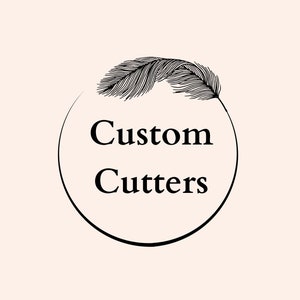 May include: A logo with the words "Custom Cutters" in a black, bold font, inside a black circular frame. A detailed black feather sits above the text, against a soft, peach-coloured background.