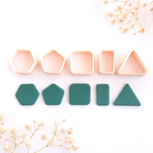 Könnte beinhalten: Eine Sammlung von geometrischen Formen-Ausstechern und passenden teal-grünen Tonformen. Die Ausstecher haben die Form eines Sechsecks, Fünfecks, Quadrats, Rechtecks und Dreiecks. Die Tonformen sind darunter angeordnet.