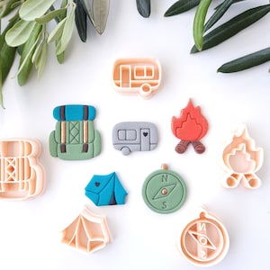 Può includere: Una collezione di formine per biscotti a tema campeggio, tra cui uno zaino, una tenda, un falò, una bussola e un camper. Le formine sono nei toni del rosa, verde, blu e grigio, perfette per biscotti a tema campeggio.