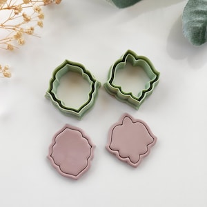 Könnte beinhalten: Vier Ausstecher in Hellgrün und Mauve. Zwei sind offene, gezackte Formen und zwei sind feste, gezackte Formen. Sie sind auf einer weißen Oberfläche angeordnet, was auf ein Back- oder Bastelthema hindeutet. Ideal für Kekse oder Dekorationen.