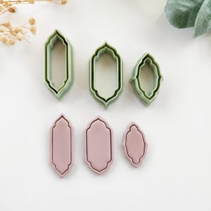 Könnte beinhalten: Ein Set aus sechs Ausstechern in einer dekorativen, bogenförmigen Form. Drei sind hellgrün und drei sind ein gedämpftes Rosa. Die Ausstecher sind in zwei Reihen angeordnet, die grünen oben und die rosa unten.
