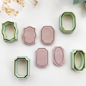 Pode incluir: Uma coleção de cortadores de biscoitos em várias formas, incluindo designs retangulares e ovais. Os cortadores são em duas cores: verde claro e rosa suave. As formas são projetadas com uma borda decorativa.