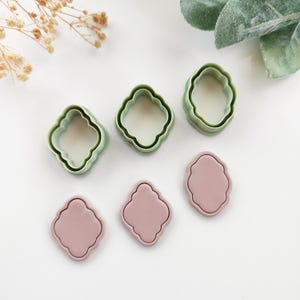 Könnte beinhalten: Eine Auswahl an Polymer Clay Ausstechern in zarten Grün- und Rosatönen. Die Ausstecher haben ein dekoratives, wellenförmiges Design, ideal für Bastelprojekte. Das Bild zeigt die Werkzeuge von oben.