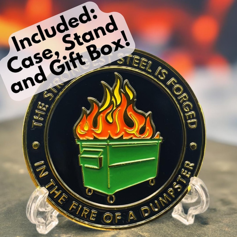 May include: A gold-colored metal coin with a black background and a green dumpster on fire. The text "THE STRONGEST STEEL IS FORGED IN THE FIRE OF A DUMPSTER" is written around the edge of the coin.
