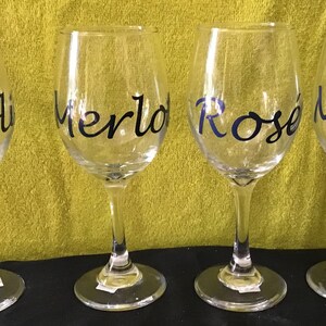 Könnte beinhalten: Vier klare Weingläser aus Glas mit schwarzer Beschriftung. Die Gläser sind mit "Chardonnay", "Merlot", "Rosé" und "Moscato" beschriftet.