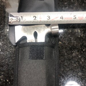 May include: A black nylon pouch with a velcro closure, containing a multi-tool with a hammer, a saw, a bottle opener, and a screwdriver. The tool is measured with a tape measure, showing it is 4 inches long.