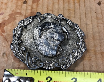 Op de afbeelding: Zilverkleurige gesp met een sierlijk ontwerp met een rammenkop in het midden. De gesp is 5 cm breed.