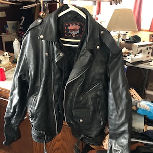 May include: Black leather motorcycle jacket with a zipper closure and a belt at the waist. The jacket has a label that reads "American Classics" with a star logo.