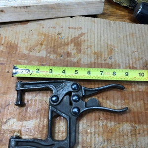 May include: A black metal C-clamp with a yellow tape measure behind it. The clamp has a label that reads "12031".