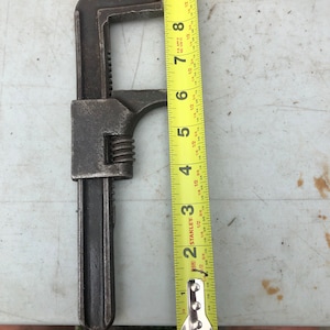 May include: A vintage adjustable wrench with a black finish and a yellow Stanley tape measure next to it. The tape measure is marked with inches and fractions of an inch. The wrench is approximately 9 inches long.