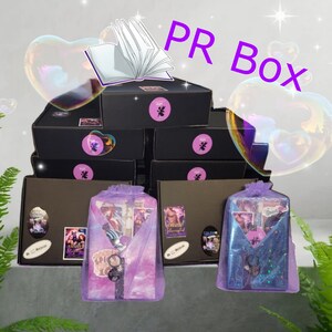 May include: A stack of black boxes with a purple and white book on top. The boxes are labeled "PR Box". Each box contains a purple and white book with a different cover. The books are wrapped in a purple and white bag.
