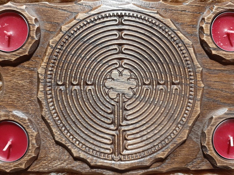 Pu&ograve; includere: Un vassoio di legno con un design a labirinto intagliato al centro. Il vassoio ha quattro portacandele ai bordi, ognuno con una candela rossa.