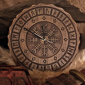 Könnte beinhalten: Eine Holzuhr mit dunkelbrauner Oberfläche. Das Zifferblatt der Uhr zeigt ein Vegvisir-Symbol, ein nordisches Richtungssymbol, umgeben von Runen. Die Zeiger der Uhr sind schwarz.