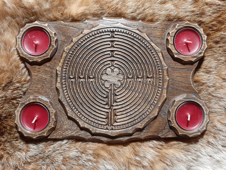 Pu&ograve; includere: Un vassoio di legno con un design a labirinto intagliato e quattro portacandele. I portacandele sono riempiti di candele rosse.