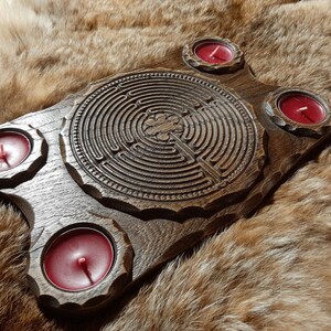 Pu&ograve; includere: Un vassoio di legno con un design a labirinto intagliato e quattro portacandele. I portacandele sono riempiti di candele rosse.
