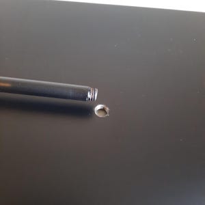 May include: A black metal rod with a threaded end is inserted into a hole in a black surface.