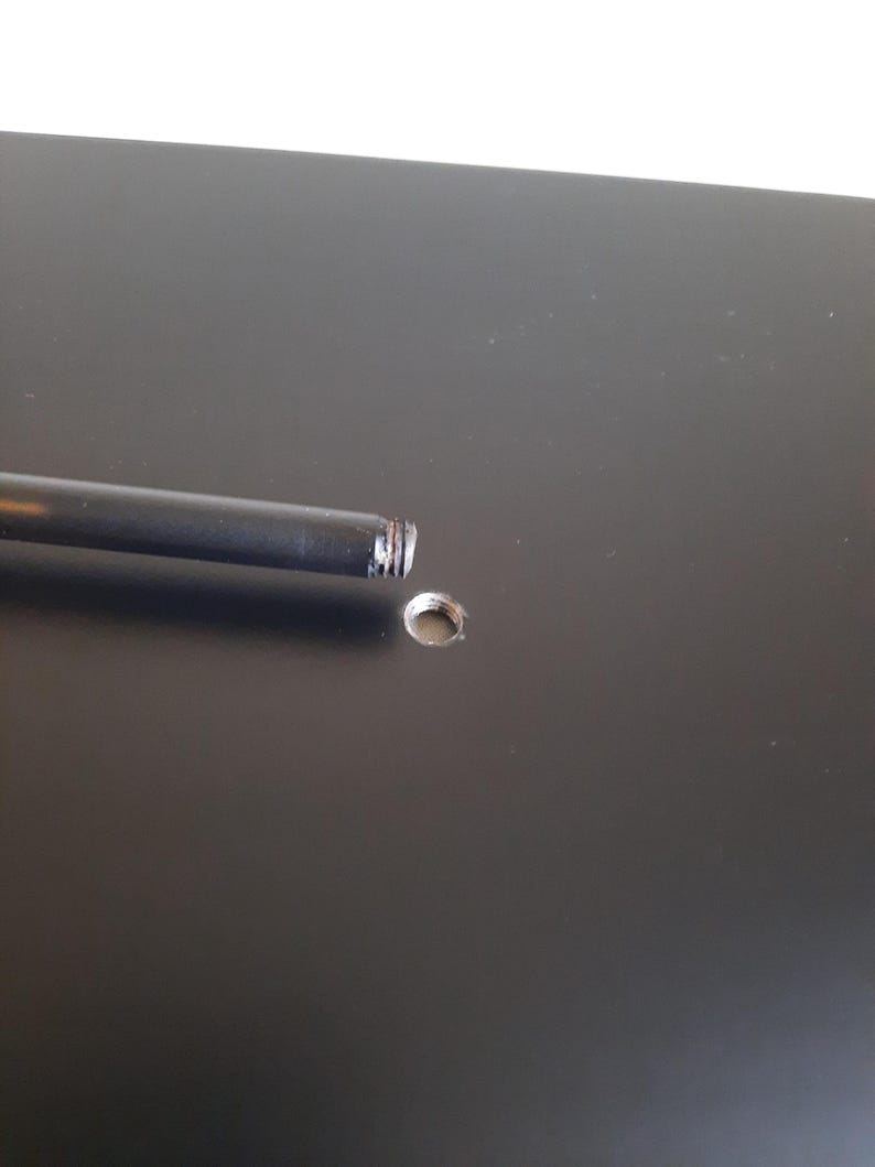 May include: A black metal rod with a threaded end is inserted into a hole in a black surface.
