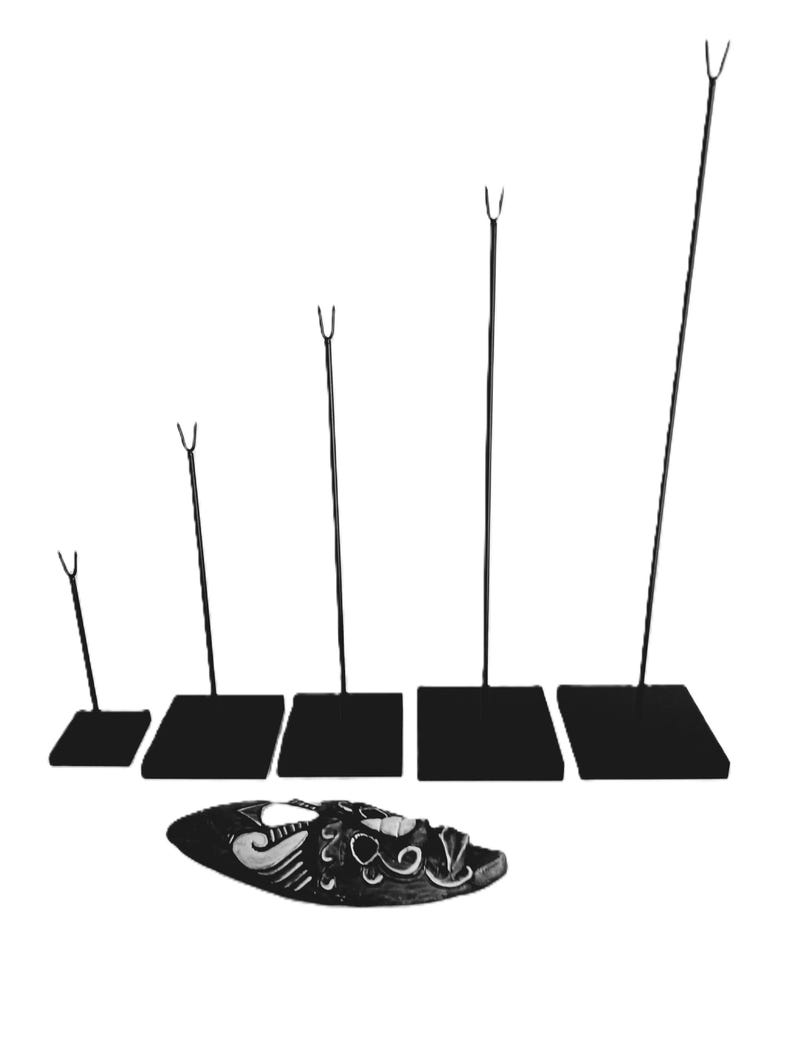 May include: Five black metal display stands with different heights, each with a square base and a forked top. A black and white mask with a decorative design is lying on the table below the stands.