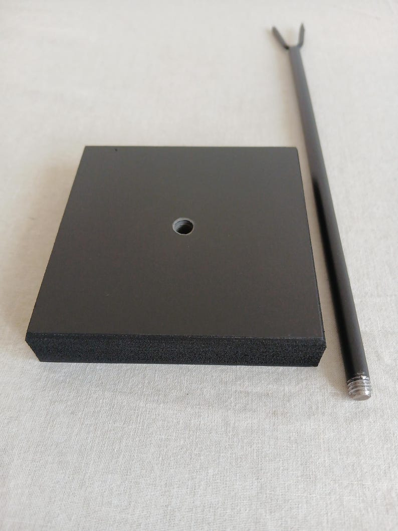 May include: A black square base with a round hole in the center and a black metal rod with a forked top.