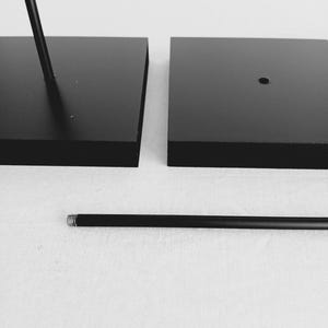 May include: Two black square bases with a black metal rod. The rod has a threaded end.