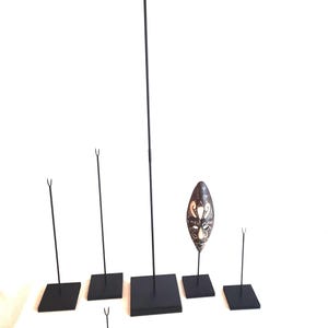 May include: Set of six black metal display stands with square bases. The stands are different sizes and are used to display objects such as masks or sculptures.