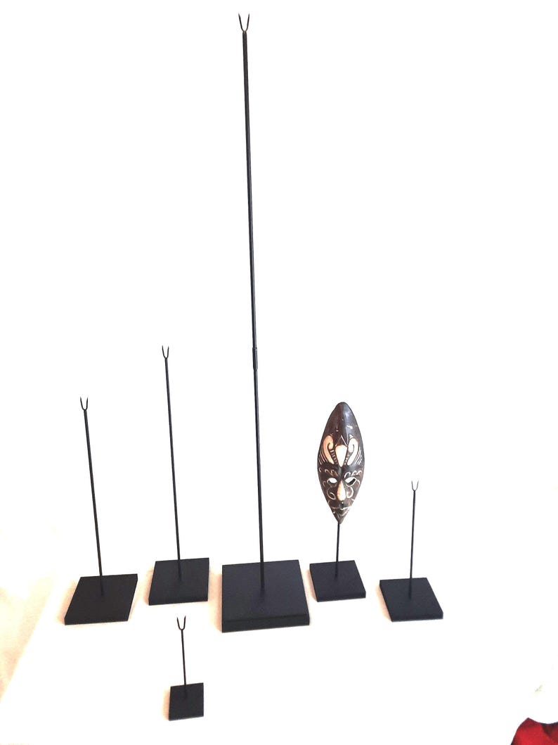 May include: Set of six black metal display stands with square bases. The stands are different sizes and are used to display objects such as masks or sculptures.