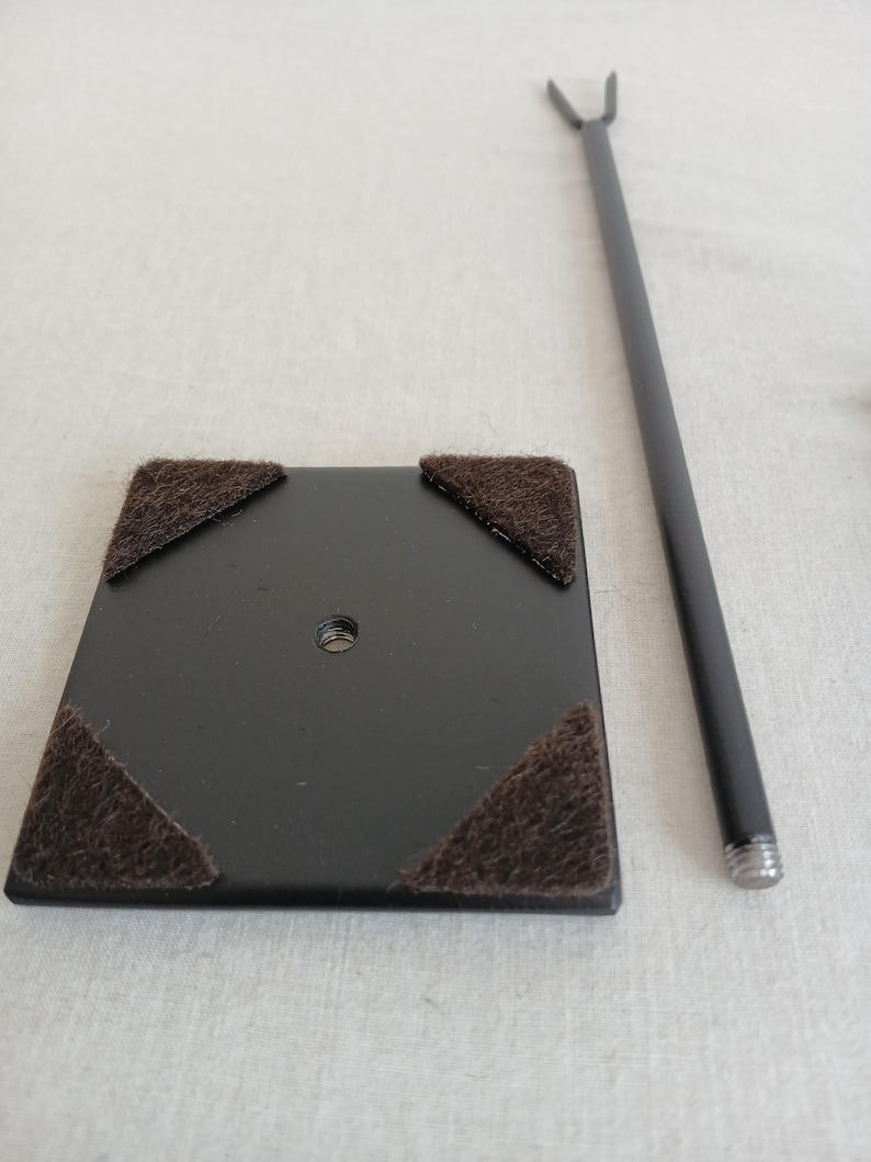 May include: Black metal display stand with a square base and four felt pads. The stand has a metal rod with a forked top.